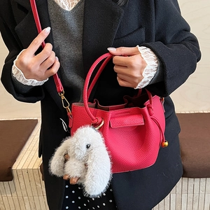 Detail of rose red lychee grain leather bucket bag with cute plush bunny charm and strap