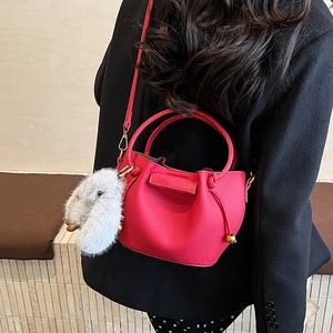 Detail of red lychee grain leather bucket bag with cute plush rabbit charm and gold hardware