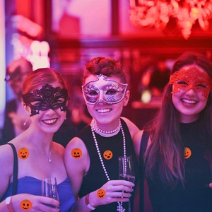 Three models wearing lace eye masks and pumpkin tattoos at a festive Halloween party