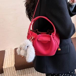 Detail of red pebbled leather bucket bag with a plush bunny charm and golden hardware