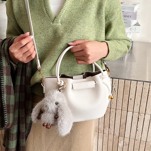 Detail of white litchi pattern bucket bag with rabbit charm and drawstring closure