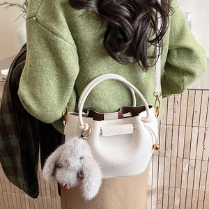 Detail of white lychee pattern bucket bag with cute plush rabbit charm and gold hardware
