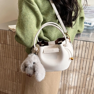Detail view of white lychee leather bucket bag with gray plush bunny charm and gold hardware