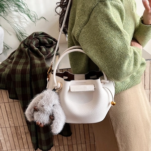 Detail view of white lychee leather bucket bag with plush bunny charm and gold hardware
