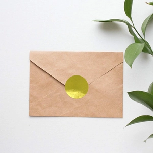 Golden round seal sticker on kraft envelope with a minimalist aesthetic greenery background