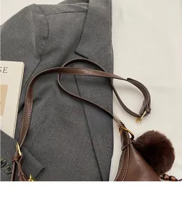 Detail view of brown faux leather shoulder bag with adjustable strap and plush pompom charm
