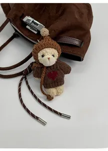 Detail of cute plush teddy bear charm in knit sweater hanging on a brown bucket bag