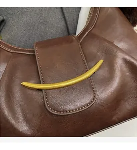 Macro detail of dark brown leather handbag with polished gold-tone curved metal buckle