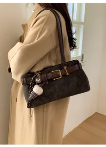 Close-up of vintage brown baguette bag with decorative buckles and plush charm on beige coat