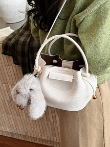 White lychee leather bucket bag with plush rabbit charm shown in a lifestyle pose