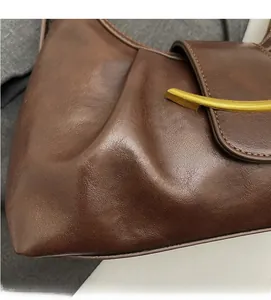 Detail of dark brown leather bag showing pleated texture and golden curved metal buckle