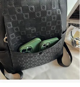Close-up of black checkered leather backpack showing spacious front pocket with two phones