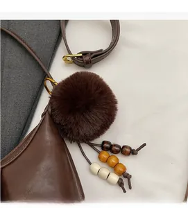 Detail of a fluffy faux fur pompom and wooden beads on a brown leather shoulder bag