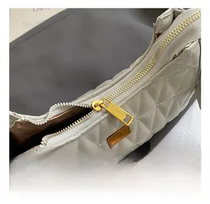 Detail shot of the golden zipper with brand engraving on grey quilted crossbody bag