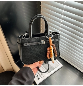 Close-up of black crossbody bag with woven texture and ethnic wooden bead charm detail