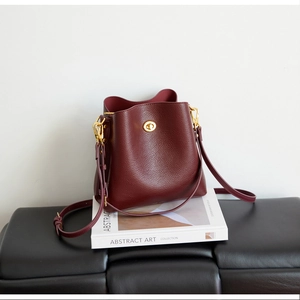 Detailed macro view of the glossy wine red bucket bag with polished golden metallic lock