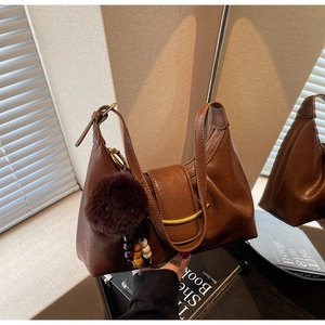 Detail of a brown leather hobo bag with gold metal buckle and fur pompom accessory