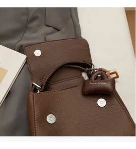 Detail of dark brown pebble leather handbag with silver magnetic buckle and mini charm