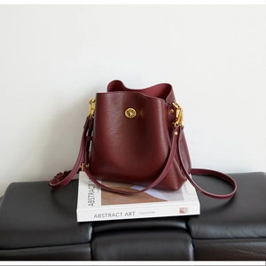 Detailed macro view of burgundy lychee leather texture and gold twist lock on bucket bag