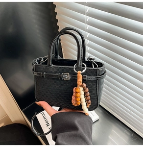 Detail of black checkered shoulder bag with decorative belt strap and beaded charm