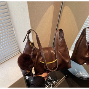 Detail of a brown leather shoulder bag with a gold metal clasp and a fuzzy ball charm