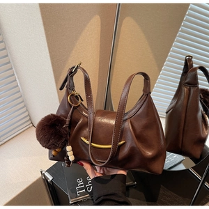 Detail of dark brown leather handbag with gold crescent clasp and plush pendant charm