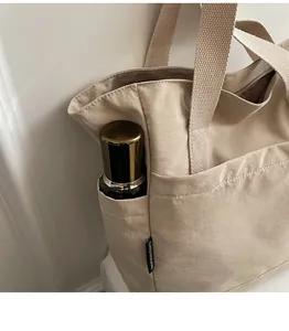 Gros plan de la poche latérale d'un cabas en toile beige avec bouteille et étiquette tissée