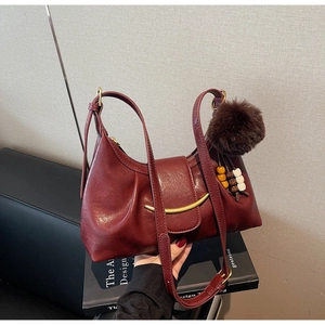 Detail of wine red faux leather handbag with ruched texture and gold crescent hardware