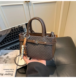 Detail of dark brown crossbody bag with checkered texture and decorative beaded keychain