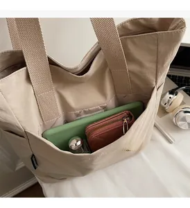 Détail de la grande poche avant du fourre-tout en nylon beige avec articles quotidiens