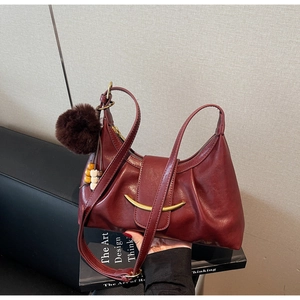 Macro detail of wine red dumpling bag texture with golden metal trim and plush charm
