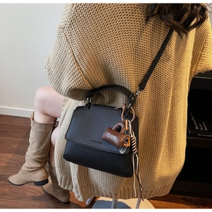 Detail of black lychee grain leather crossbody bag featuring a branded mini charm pendant