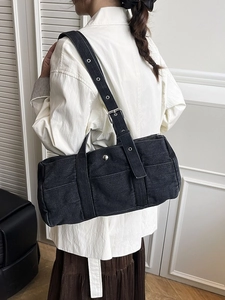 Retro black denim tote bag with silver eyelet strap shown on model in minimalist room