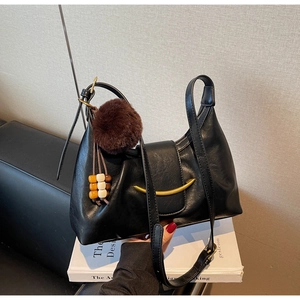 Detail of black faux leather shoulder bag with gold metal buckle and plush charm decoration