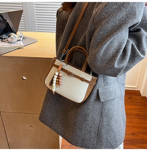 Detail of white woven crossbody bag with brown leather trim and wooden bead charm