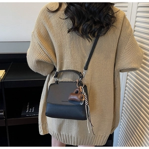 Detail of black pebbled leather crossbody bag featuring a chic brown plush bag charm
