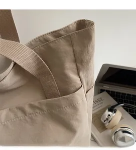 Détails des poignées larges et des poches latérales sur un grand sac cabas beige