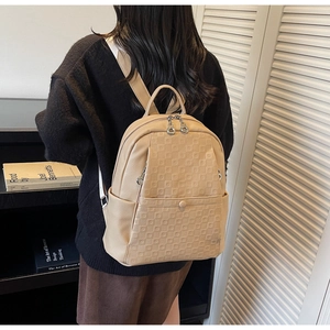 Rear view of a beige textured leather backpack on a person in a cozy interior setting