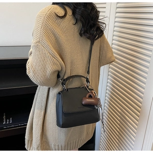 Detail of black pebbled leather handbag with silver lock and brown miniature bag charm