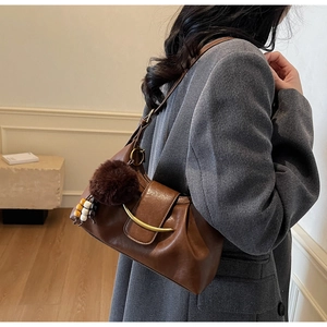 Detail of dark brown dumpling bag with golden buckle and plush charm on grey blazer