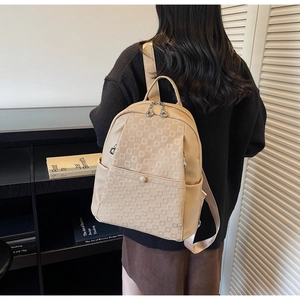 Detail of beige textured backpack with geometric embossed pattern and dual metal zippers