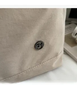 Détail du sac cabas en toile beige montrant le logo métallique CM et les coutures soignées