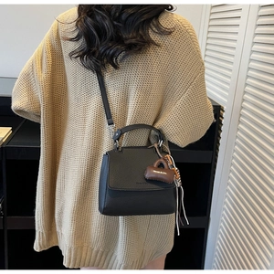 Detail of black lychee grain leather crossbody bag with a brown mini pouch charm