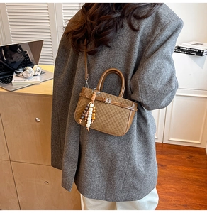 Detail of a brown checkered handbag with beaded charm and thin shoulder strap