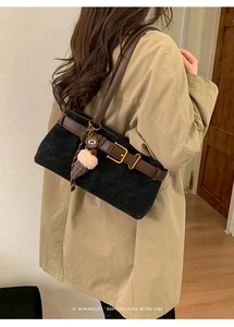 Detail of retro underarm bag in black suede and brown leather on model in beige coat