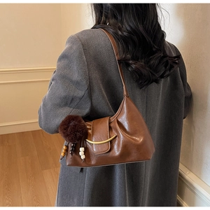 Detail of dark brown faux leather shoulder bag with gold buckle and plush charm