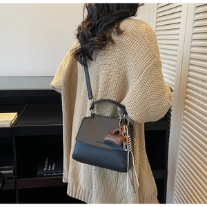 Detail of a black pebbled leather crossbody bag featuring a unique brown mini bag charm