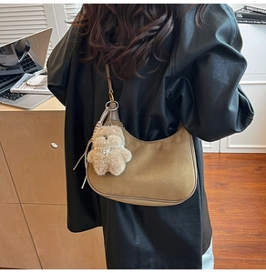 Brown suede half-moon shoulder bag with plush bear charm worn with a black leather jacket