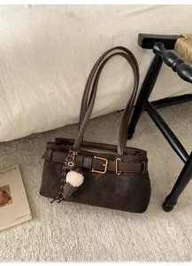 Detail of dark brown baguette bag with golden buckle and plush charm on white bedding