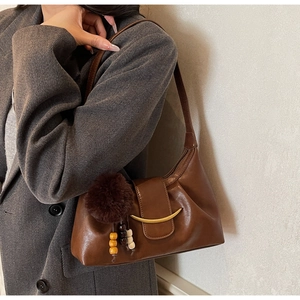 Detail of a brown leather shoulder bag with gold hardware and a decorative plush charm